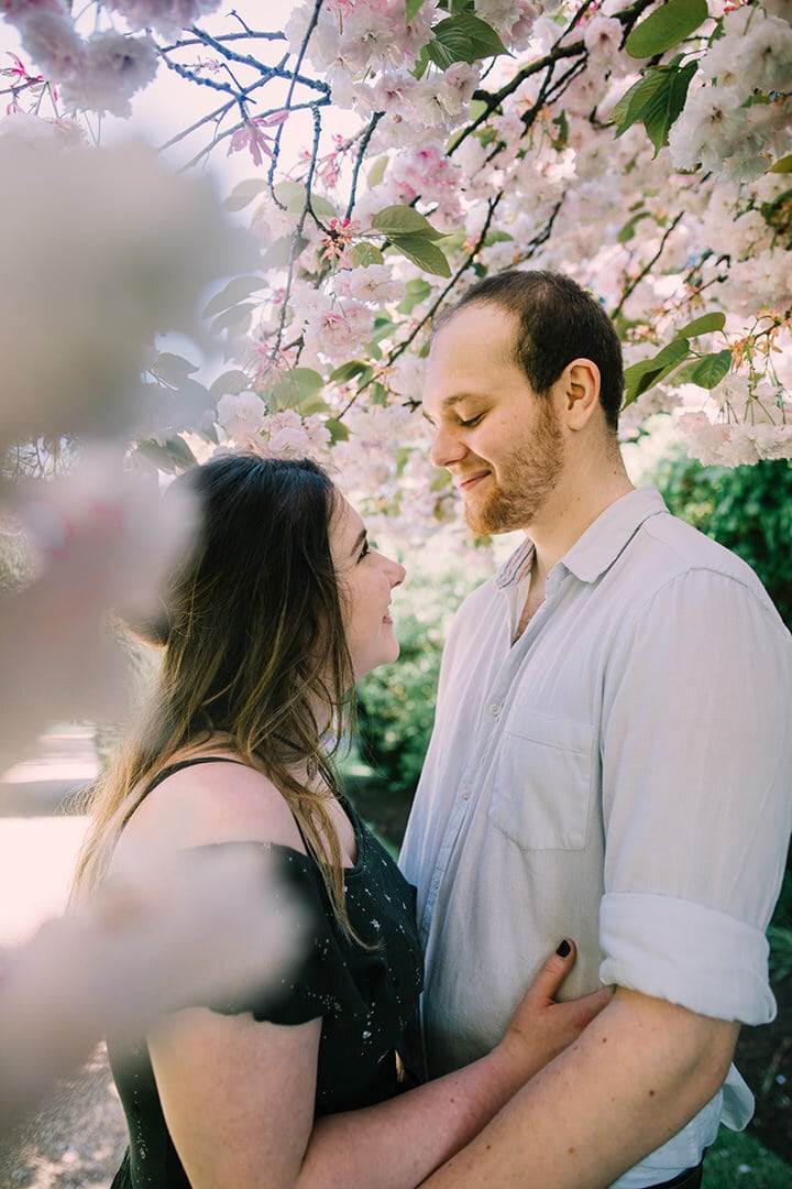 couple romantically gazing at each other under blossom trees in castle ashby's gardens