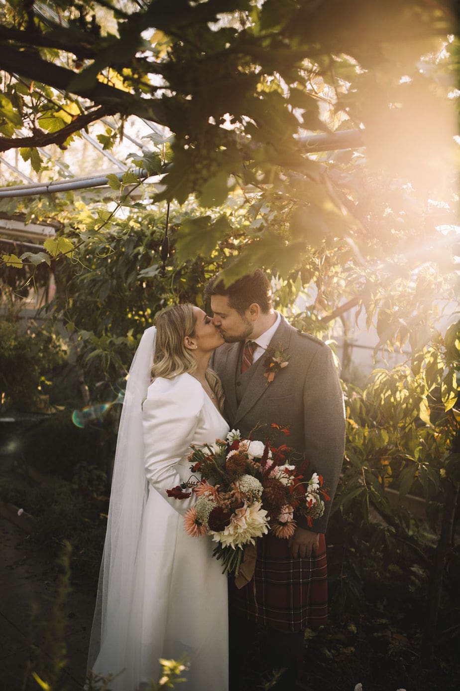 Bride and groom kissing between the greenery at the secret herb garden during their micro wedding in Edinburgh.
