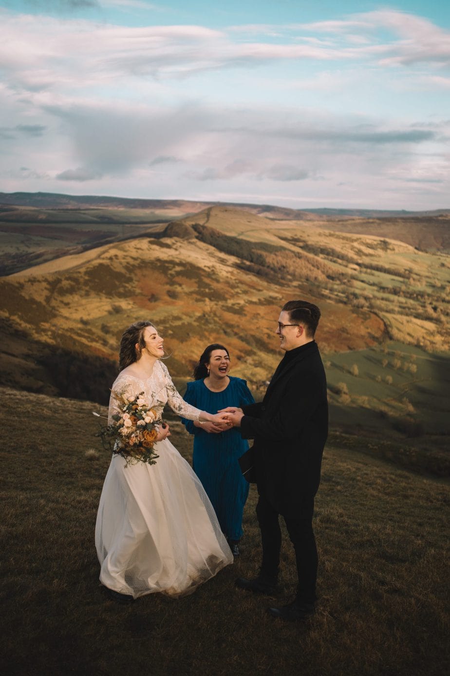 Couple laughing together with their celebrant during their elopement on Mam tor in the peak district.