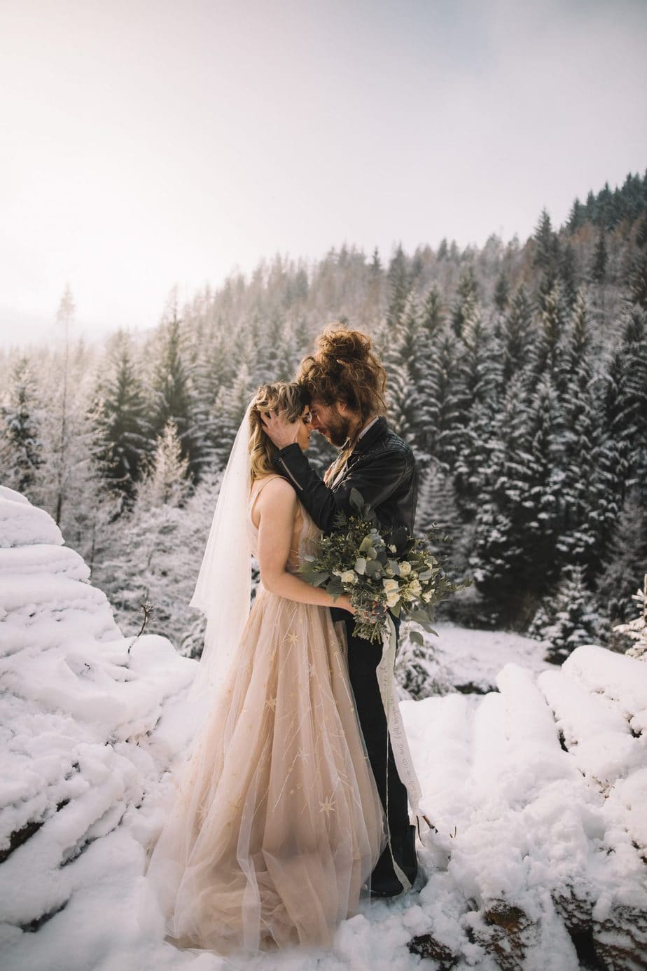 Groom holding his brides face with a snowy snake pass woodland in the background.
