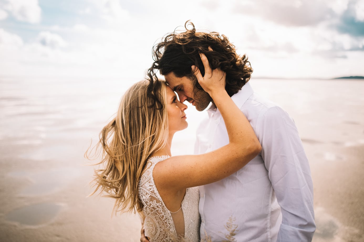 Bride and groom on a beach looking lovely at each other with the sun behind them.