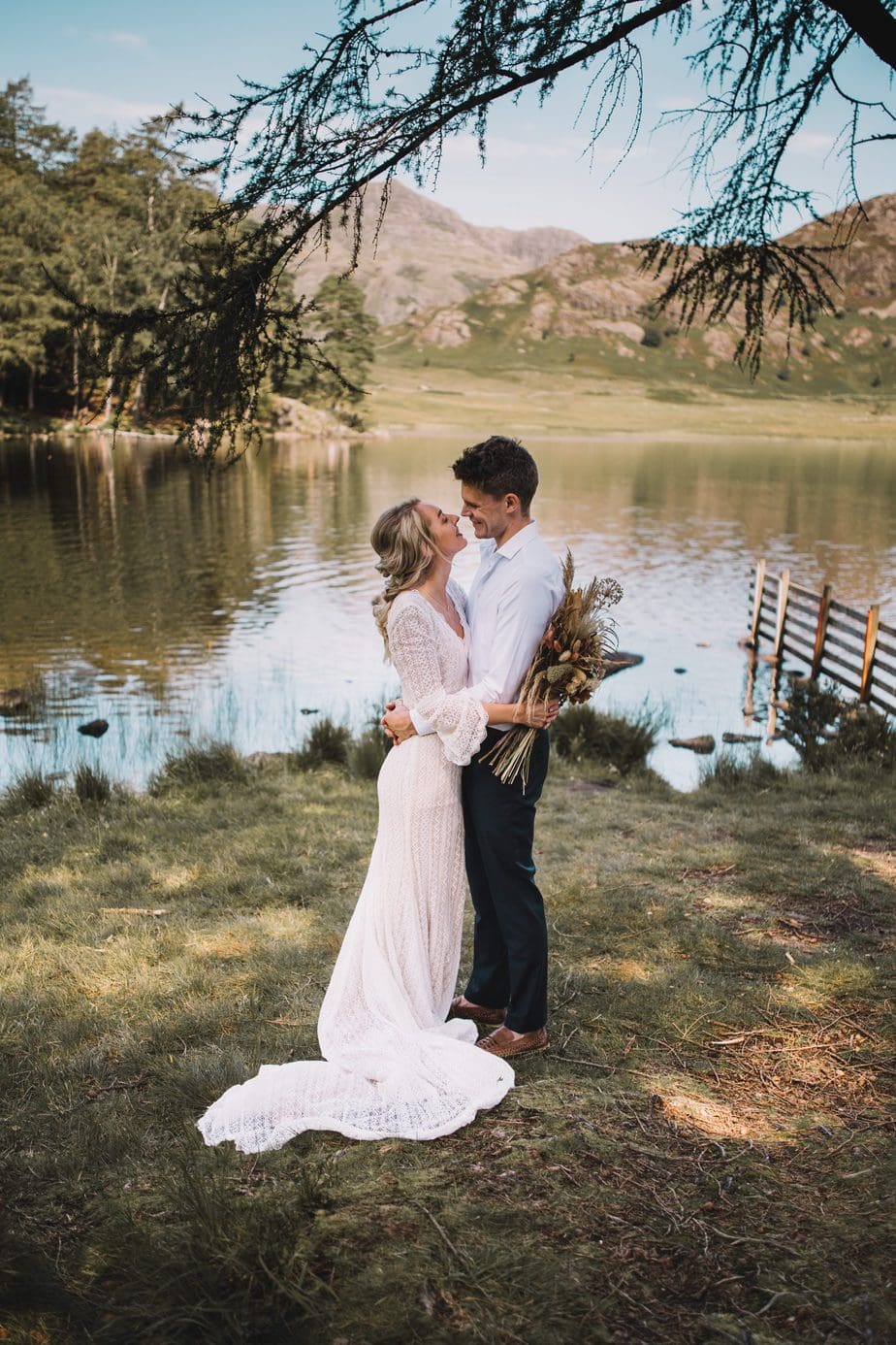 Couple cuddling with Blea Tarn lake in the background. During the Lake District elopement