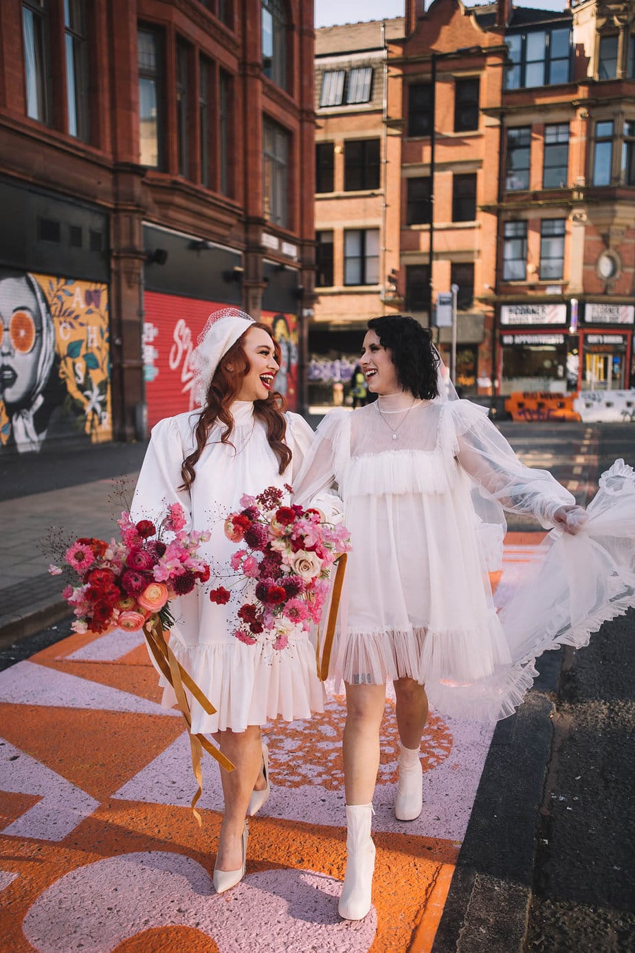 Manchester City elopement with two brides. Brides are holding hands while laughing at each other while walking down a painted street in Manchester during their elopement