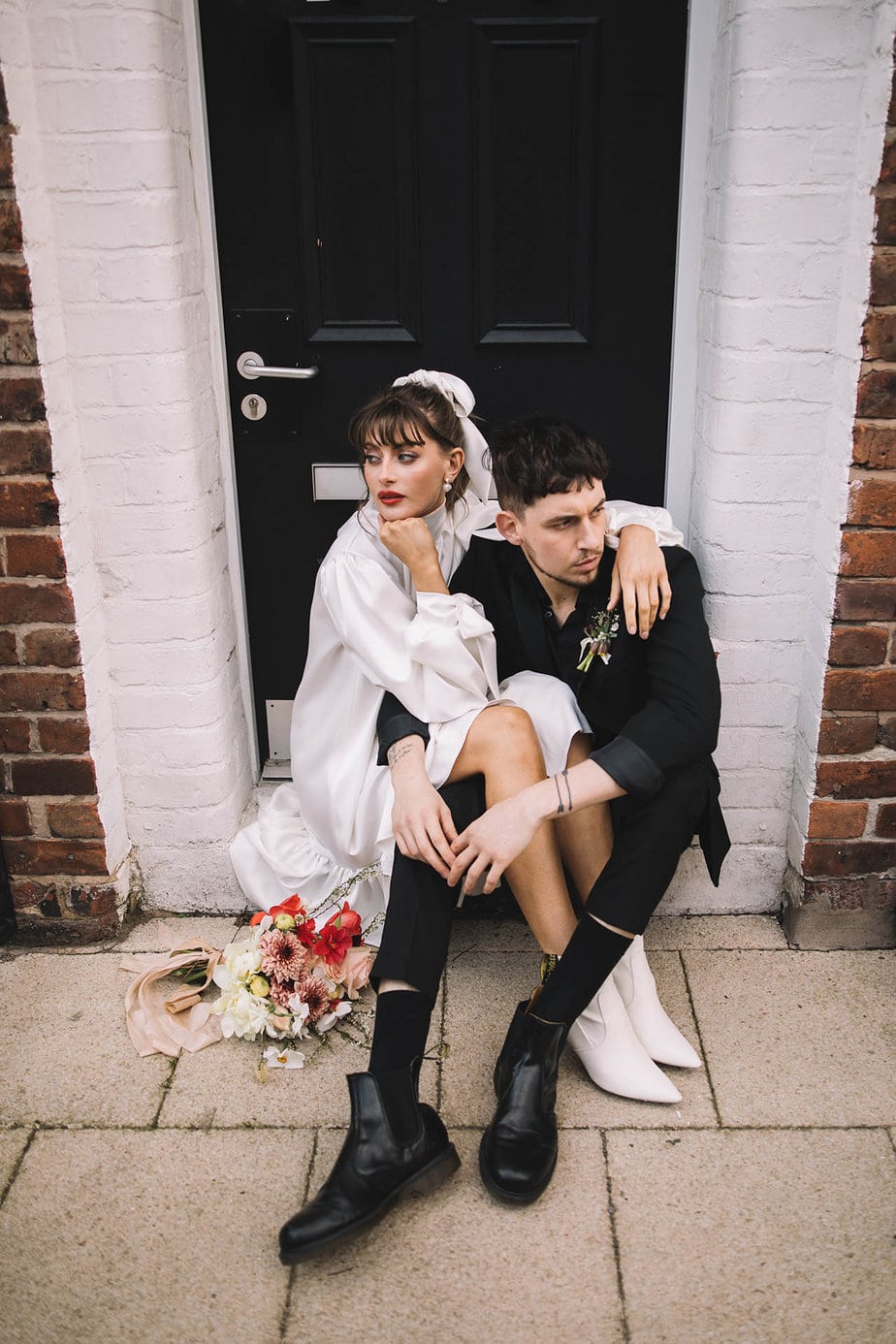 Couple sitting together on a step during their elopement day, bride wears a short white dress