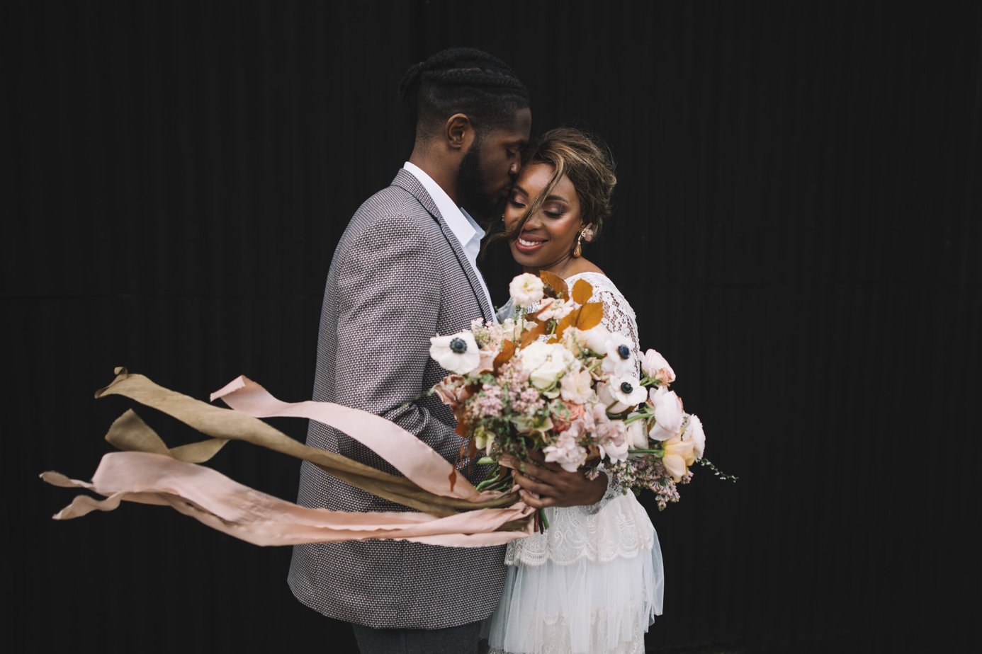 Groom kissing bride on the cheek, bride wears a Katyakatya dress and holds bouquet at woolas barn