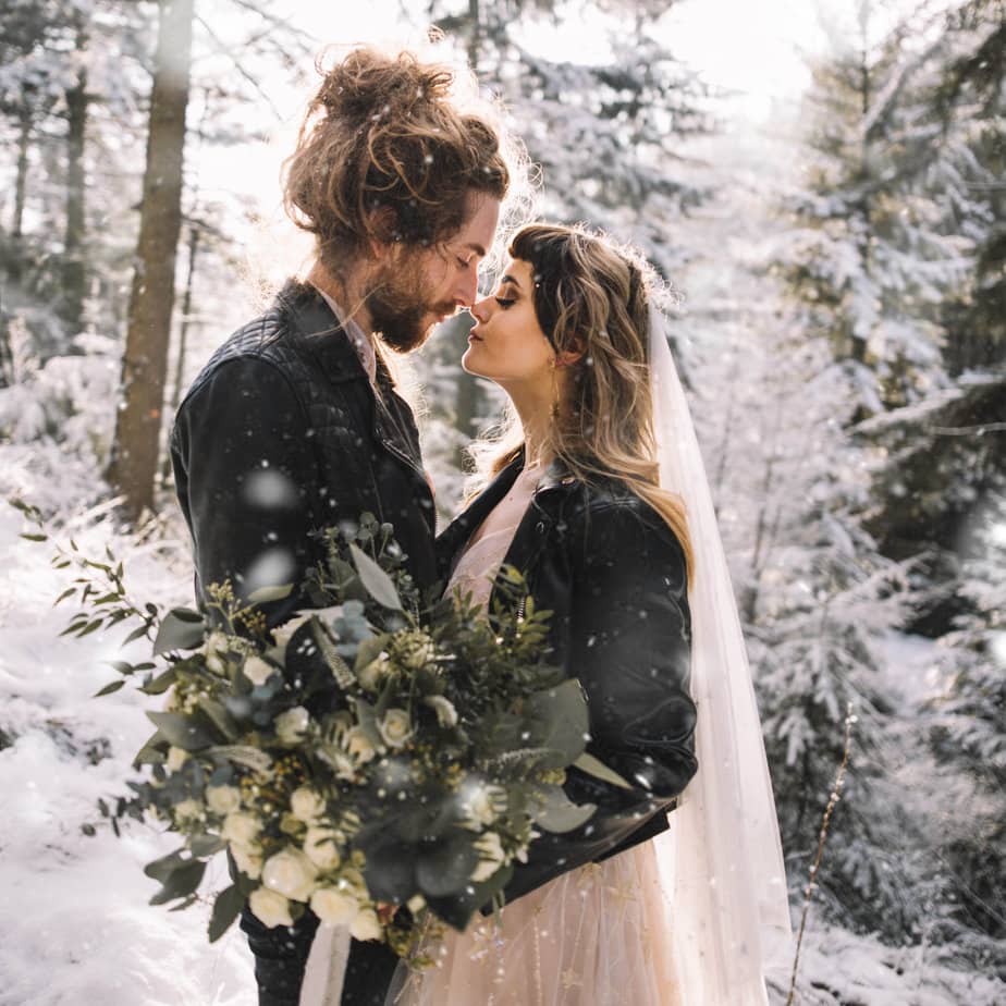 Snowy elopement shoot where couple are touching noses in a forest while it snows - featured on my how to elope in the uk blog
