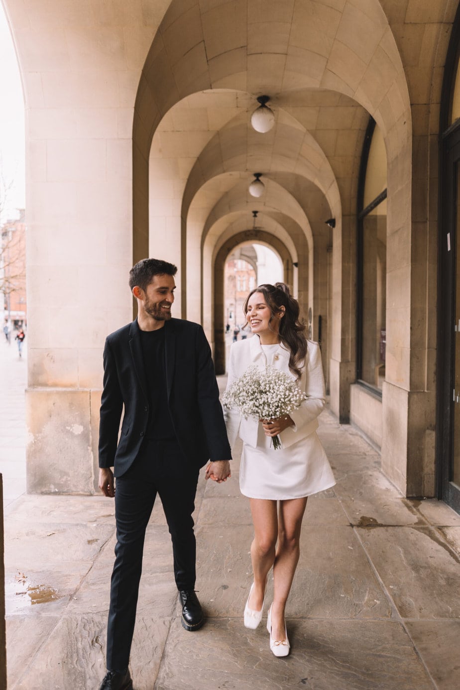 Bride and groom walking through the arches at central library before going to their small manchester wedding.