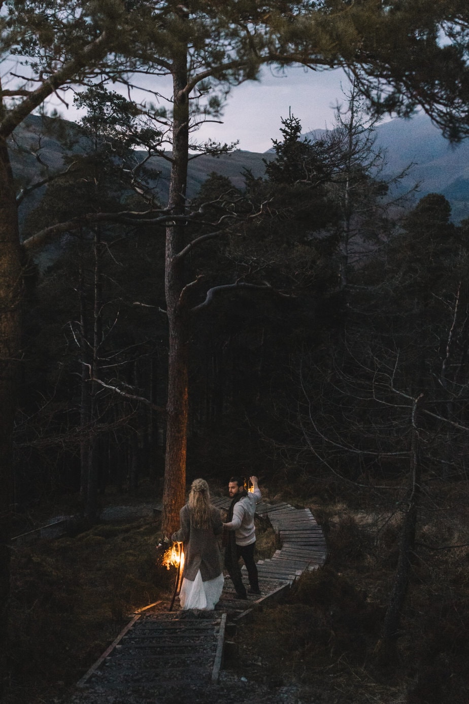 Couple carrying lanterns as they make their way back through a forest after eloping in the Lake District