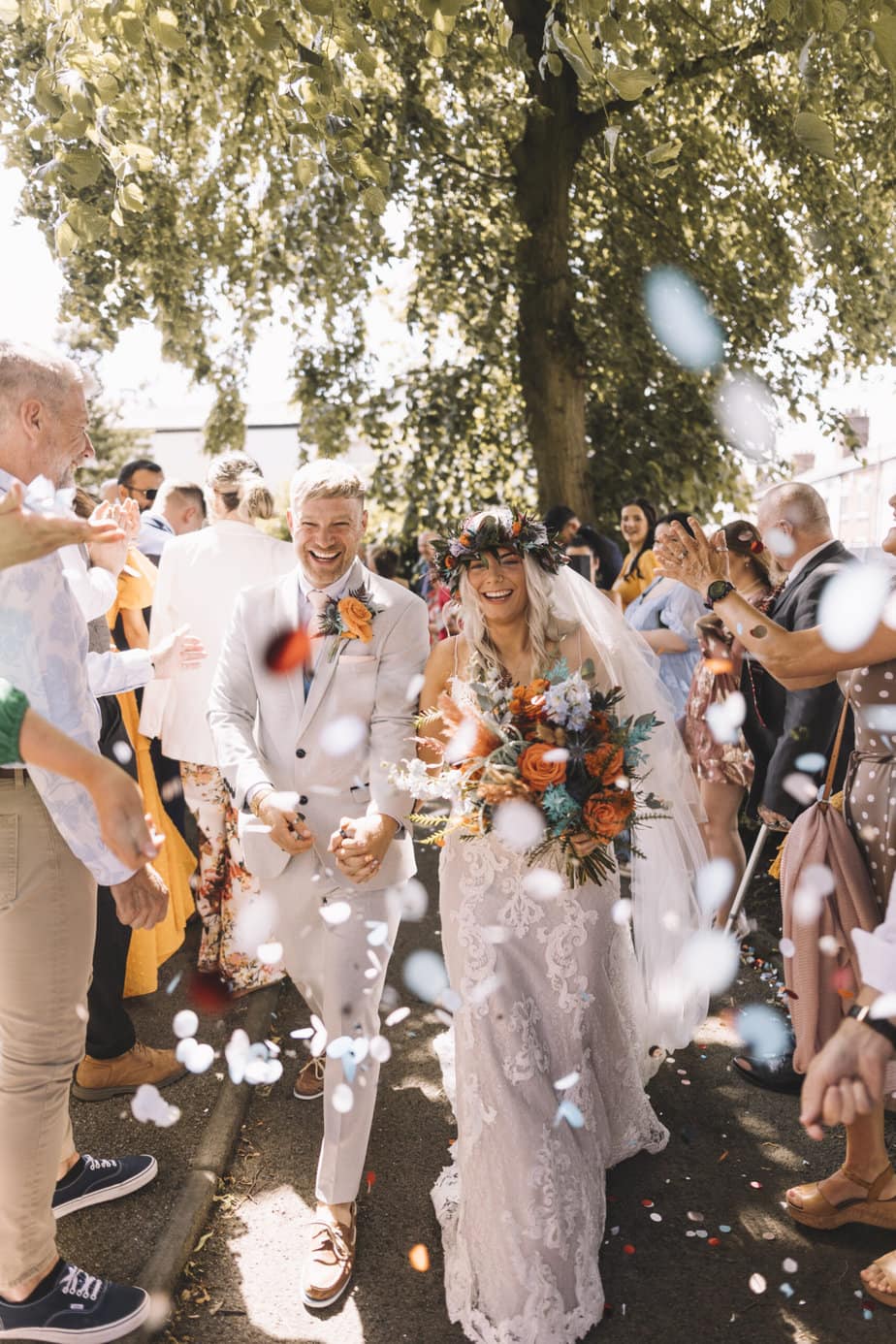 Bride and groom walking as their guests throw confetti outside Peak District church.