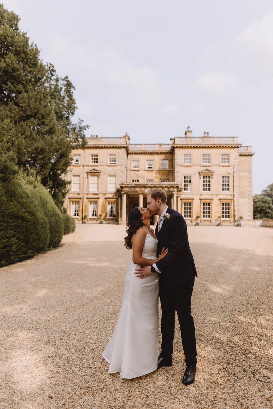 Groom kissing bride on the cheek as they stand in the doorway of Calke Abbey's orangery on their wedding day.
