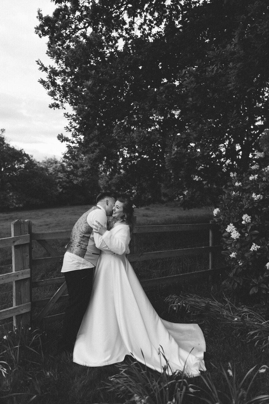 Bride and groom spraying Prosecco at camera with vintage red car and peak district farm in the background.
